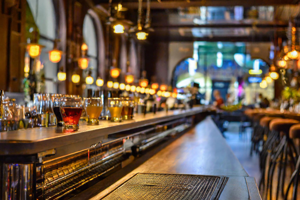 Several glasses lined up on a bar counter with stools nearby.